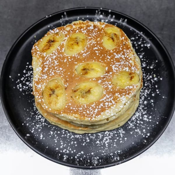 Stack of banana pancakes dusted with powdered sugar on a black plate.