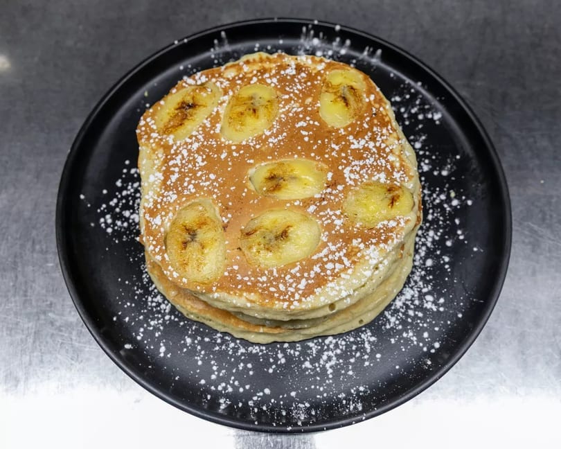 Stack of banana pancakes dusted with powdered sugar on a black plate.