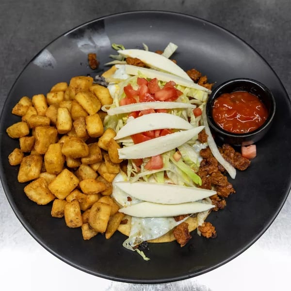 Breakfast plate with crispy home fries, huevos rancheros topped with cheese, lettuce, and tomatoes, and a side of salsa.