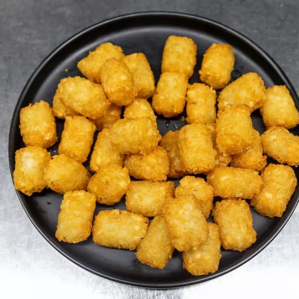 A black plate filled with golden-brown, crispy tater tots on a metallic surface.