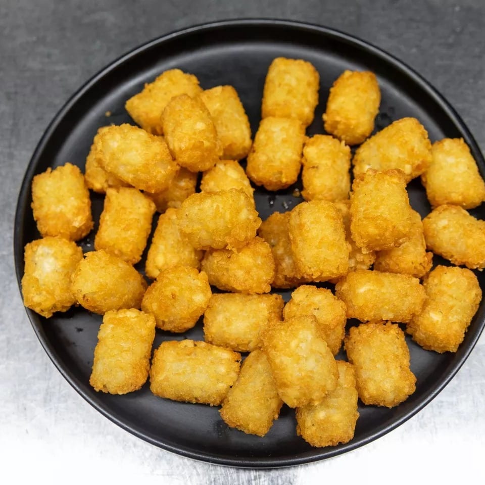 A black plate filled with golden-brown, crispy tater tots on a metallic surface.