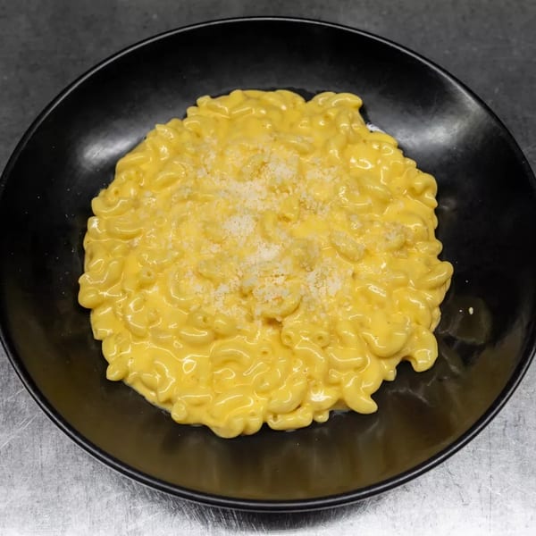 A black bowl filled with creamy macaroni and cheese, topped with grated white cheese.