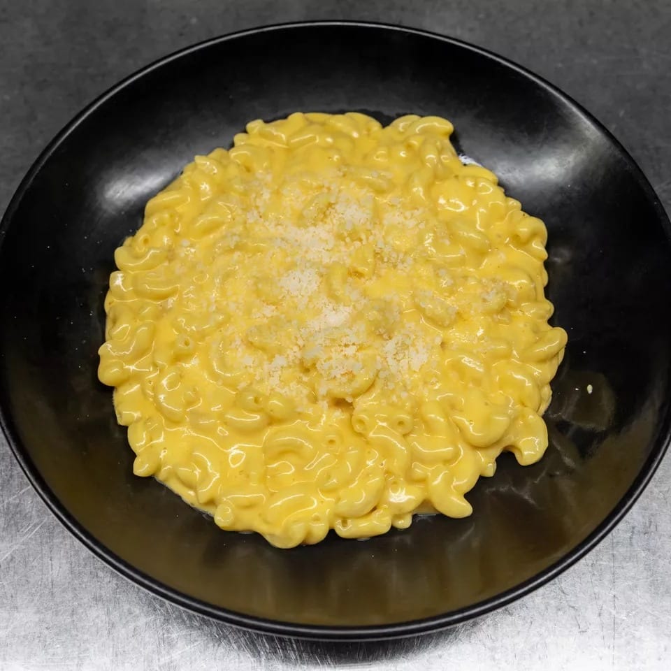 A black bowl filled with creamy macaroni and cheese, topped with grated white cheese.