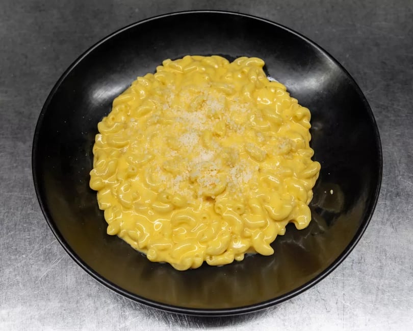 A black bowl filled with creamy macaroni and cheese, topped with grated white cheese.