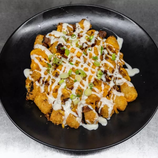 Loaded tater tots with melted cheese, bacon, ranch, and green onions on a black plate.