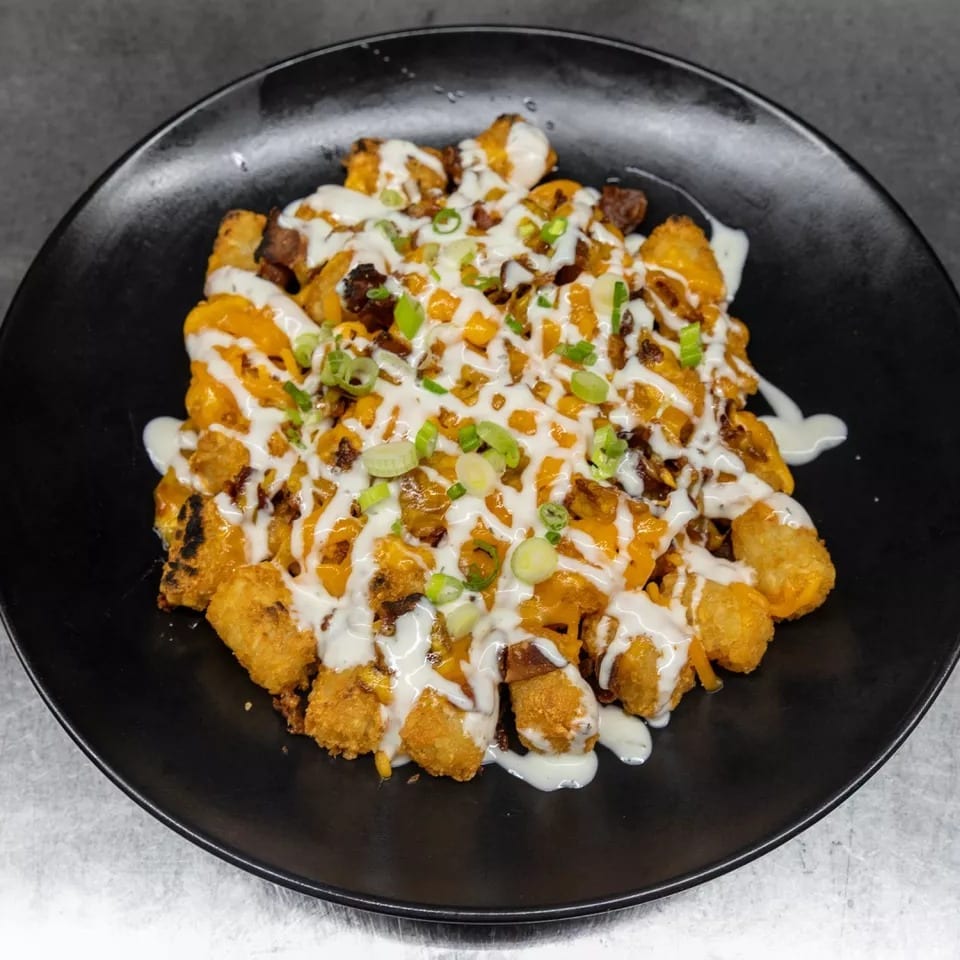 Loaded tater tots with melted cheese, bacon, ranch, and green onions on a black plate.
