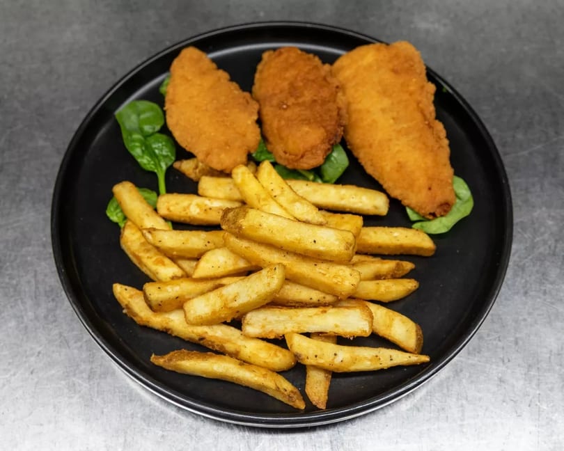 Crispy chicken tenders and golden french fries served on a black plate with a bed of spinach.