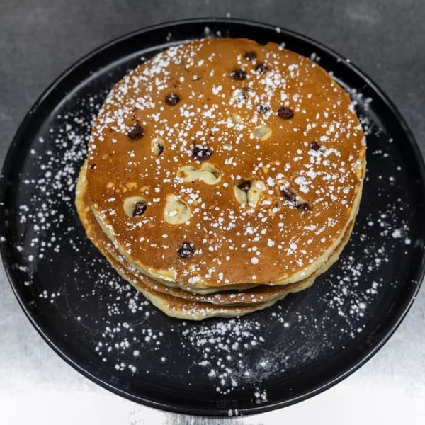 Stack of chocolate chip pancakes dusted with powdered sugar on a black plate.