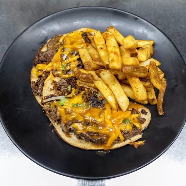 Open-faced cheesesteak sandwich with melted cheddar, green onions, and a side of golden fries.