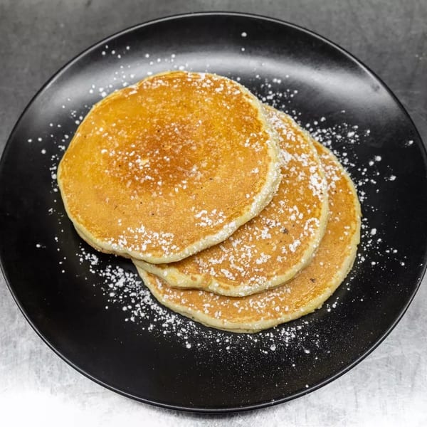 Three golden pancakes dusted with powdered sugar on a black plate.