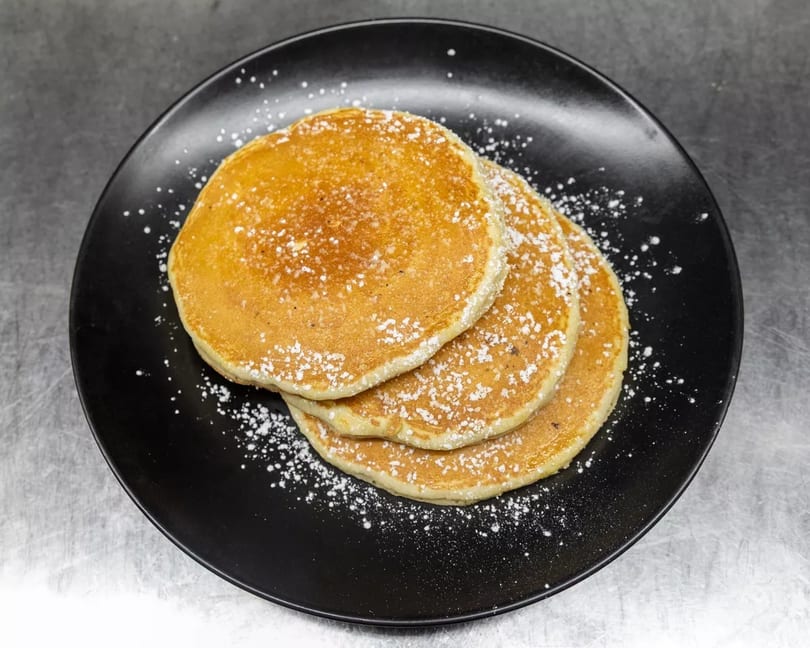 Three golden pancakes dusted with powdered sugar on a black plate.