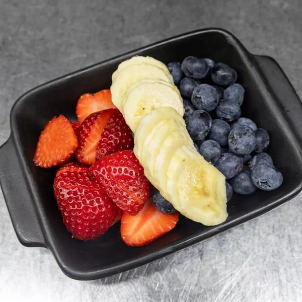 A black rectangular dish filled with fresh sliced strawberries, banana, and blueberries on a gray surface.
